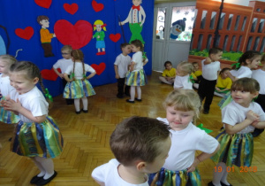Dzieci ubrane odświętnie tańczą w parach na tle dekoracji dla Dziadków.